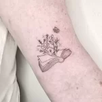 fine line book tattoo with wildflowers growing out of the pages and a butterfly above.
