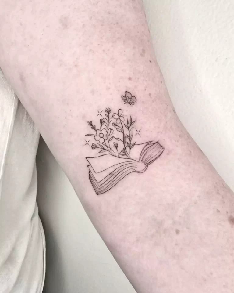 fine line book tattoo with wildflowers growing out of the pages and a butterfly above.