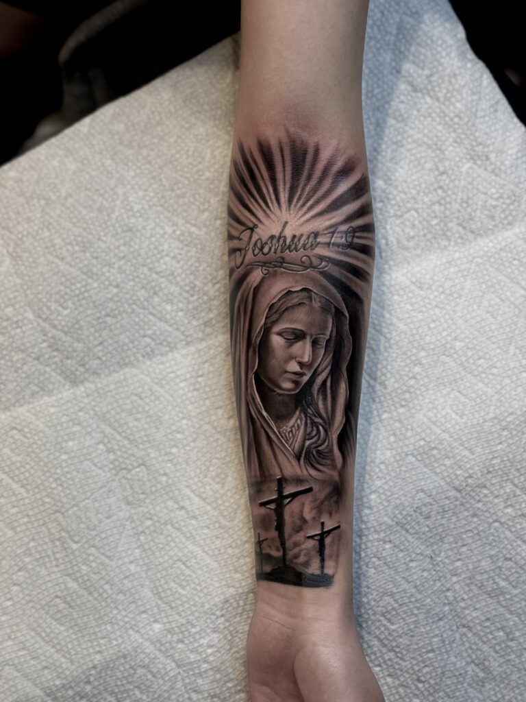 Black and white Virgin Mary of sorrows tattoo with the scene of the crucifixion of Christ and prisoners below. Above in text is Joshua 1:9 in reference ot the biblical passage